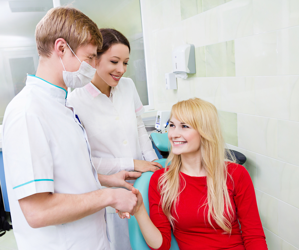 Closeup portrait dentist, doctor, assistant congratulate happy, smiling patient for successful operation procedure, isolated background clinic office. Patient visit treatment, satisfaction. Expression-1